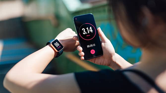 A woman using a fitness app on her smart phone and smart watch. Fitness tracking apps provide one example of the potential positive effects of technology on health.