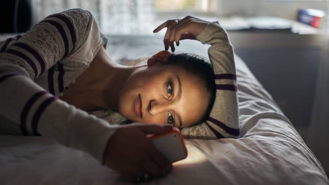 What does TBH mean? Image shows a young woman lying on her bed, looking at her phone.